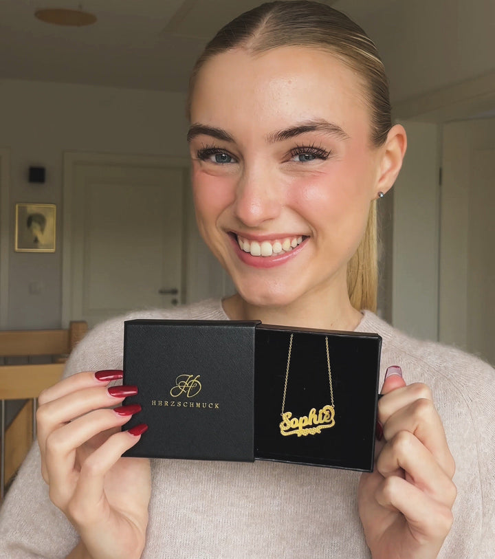 Woman smiling and holding a black box with a gold Bold Underlined Name Necklace inside