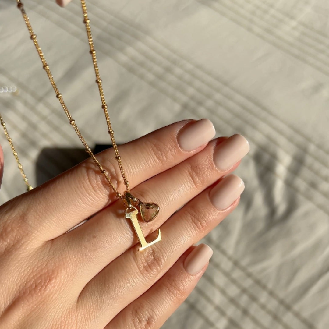 Gold personalized letter necklace with birthstone pendant displayed on hand with manicured nails.