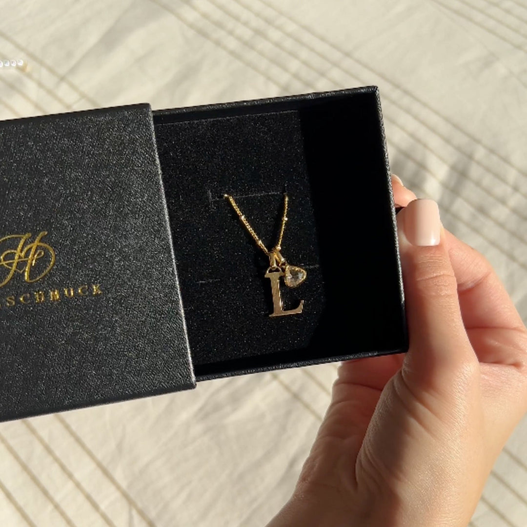 Personalized letter necklace with birthstone pendant in a black box, gold initial "L" and sparkling birthstone charm, held by hand.