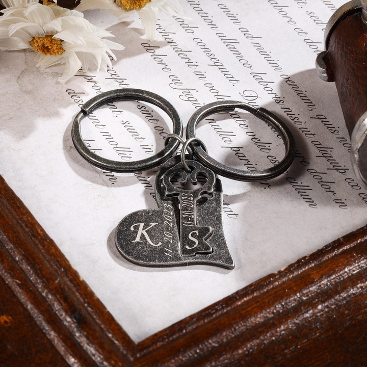 Personalized Couple's Keychain Set with Dark Grey Heart and Key Charms Engraved with Initials on a Wooden Surface