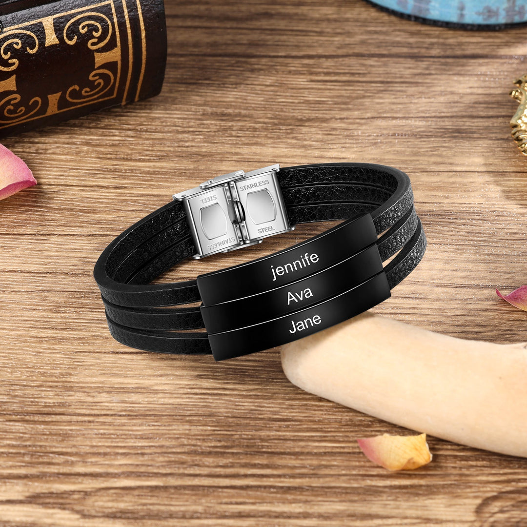 Customizable black leather bracelet with three engravings shown on a wooden surface, featuring names Jennifer, Ava, and Jane.