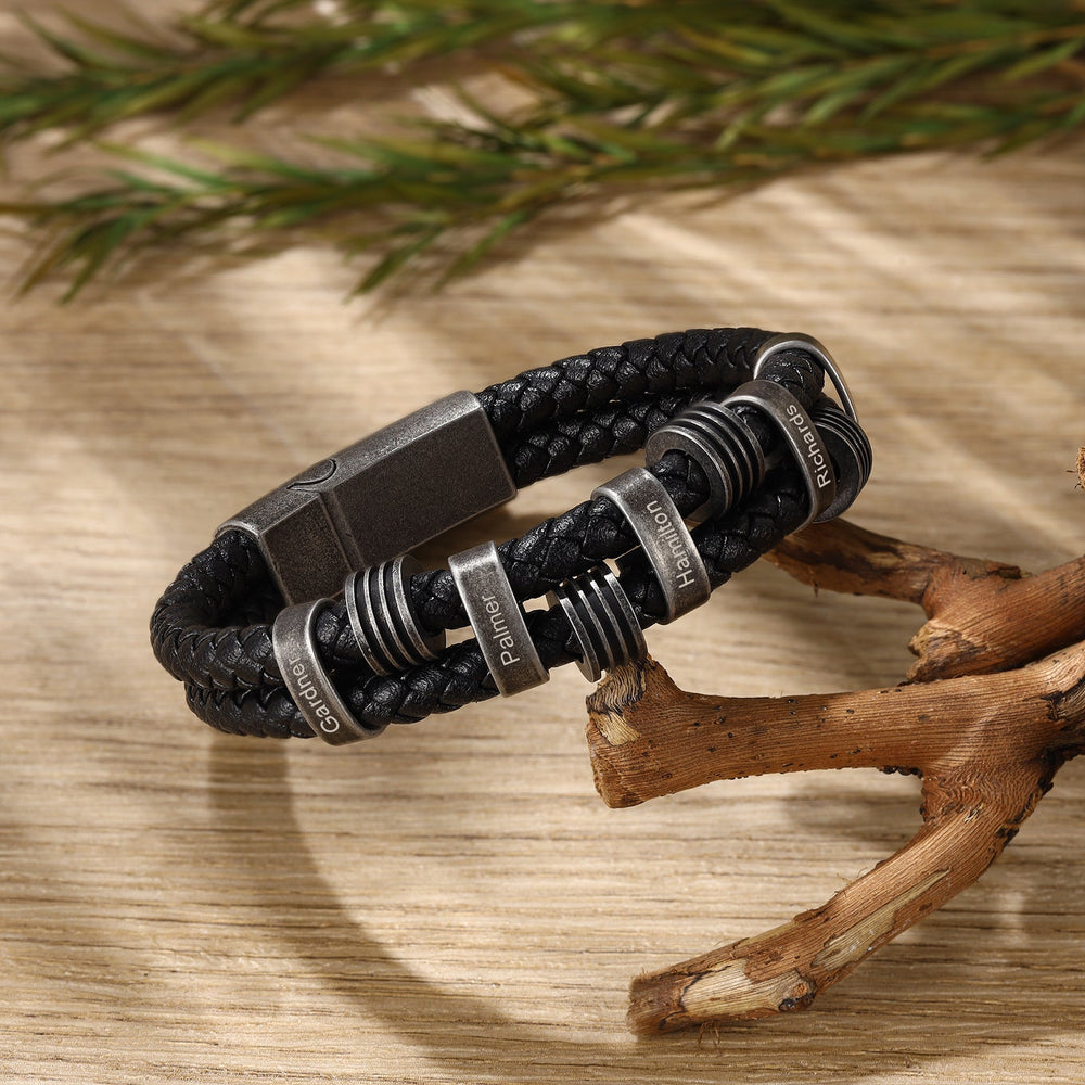 Personalized black braided leather bracelet with dark grey stainless steel rings for engravings on wooden surface background.