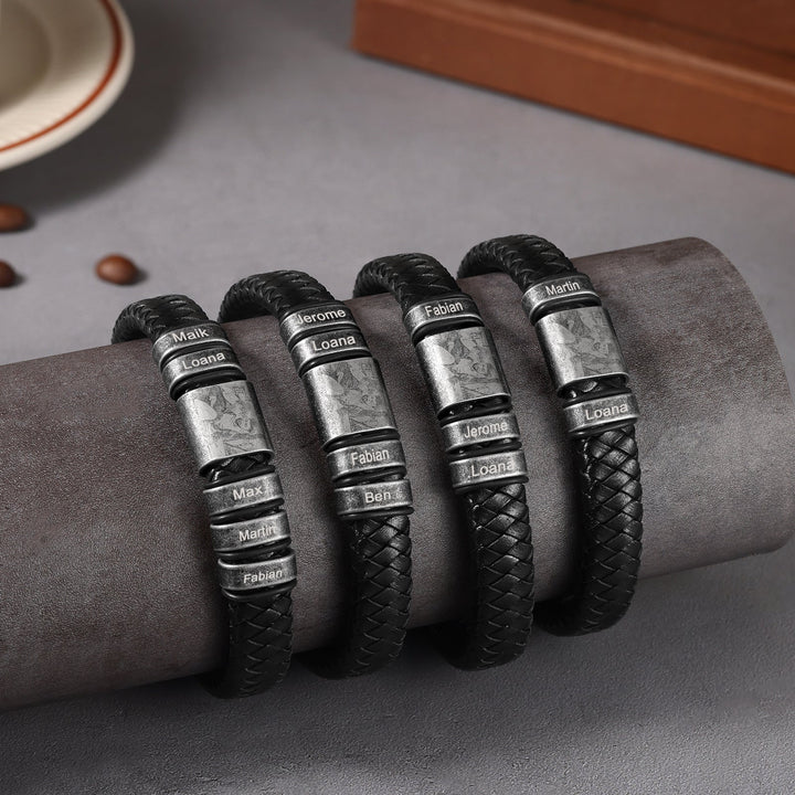 Black leather bracelets with personalized engravings and photos on stainless steel clasps, displayed on a grey cushion.