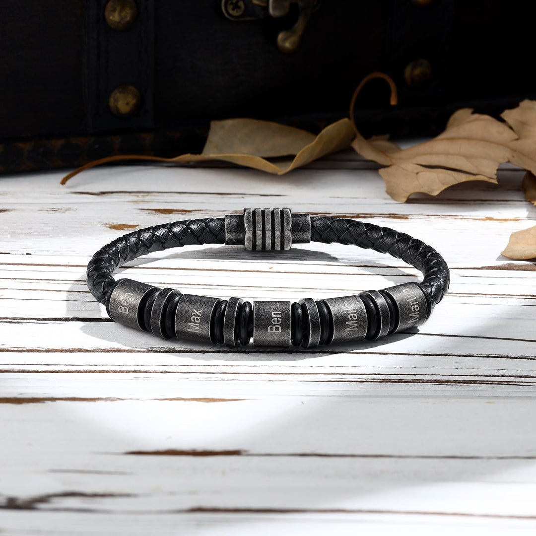 Simple vintage black braided leather bracelet with personalized engraving rings resting on a wooden surface.