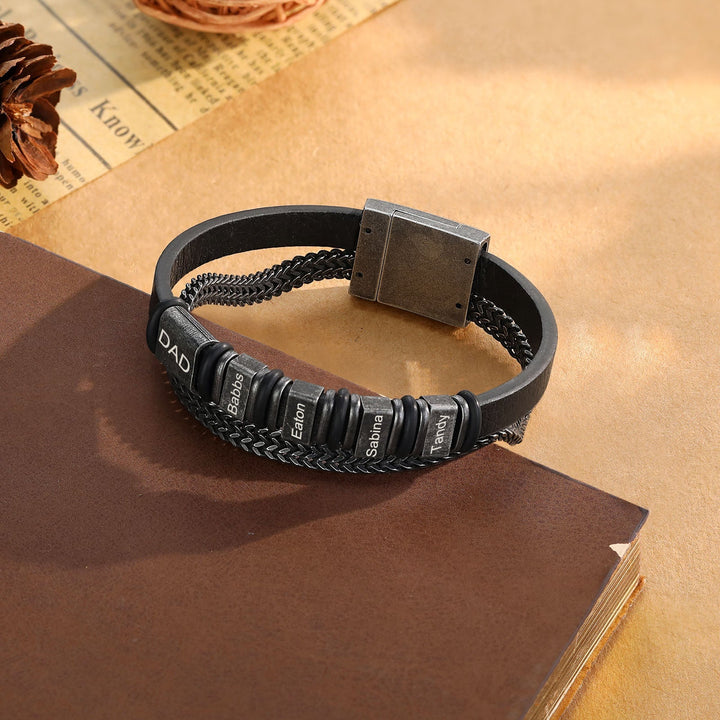 Personalized black leather bracelet with stainless steel chain and three engravings on a wooden surface.