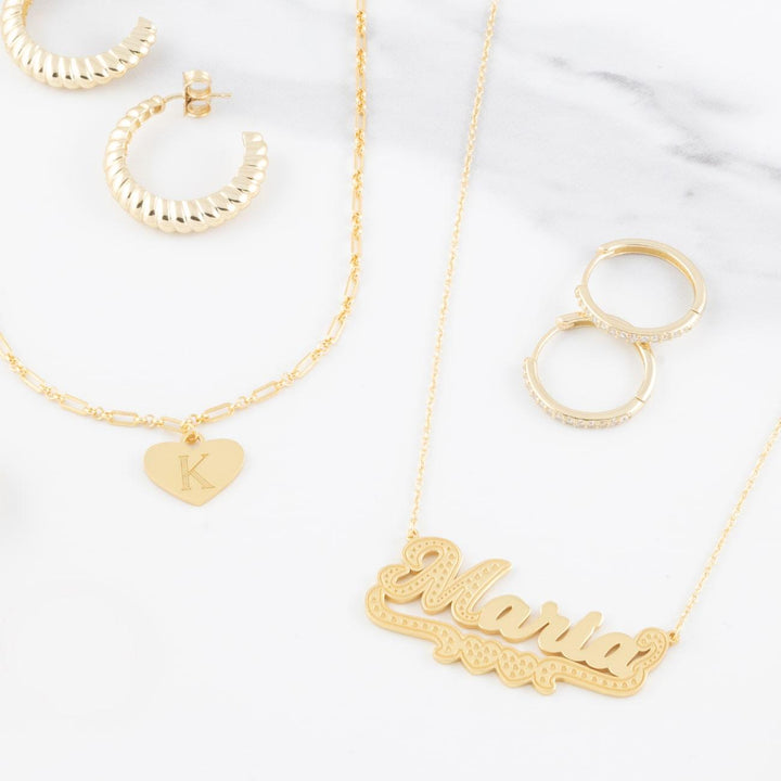 "Bold underlined name necklace 'Maria' in gold, displayed with matching gold earrings and heart initial necklace on a white background"