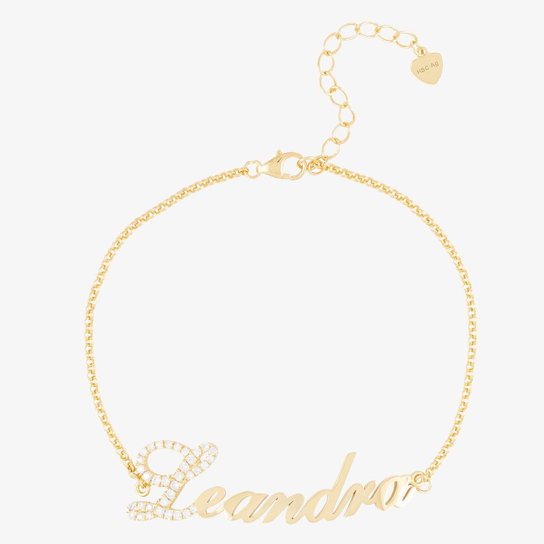 Gold personalized name bracelet with crystal accents highlighting the first letter, elegant and luxurious jewelry piece with chain and heart detail.