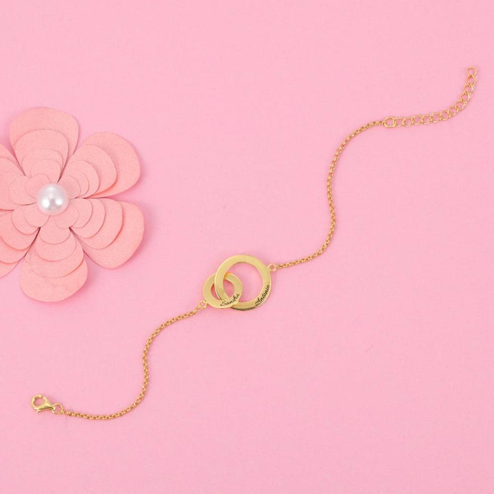 Personalized double ring bracelet in gold on a pink background with a paper flower decoration