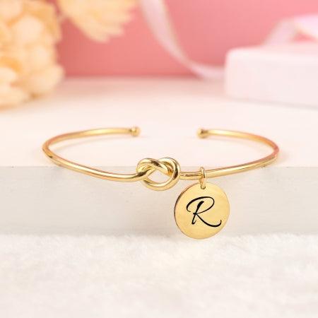 Personalized Initial Disc Bracelet in gold with engraved letter R displayed on a white surface. Chic jewelry for personal style.