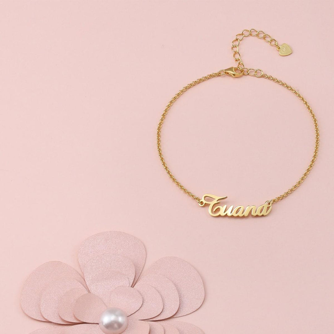 Personalized sterling silver name bracelet in gold color on a pink background with a flower accent