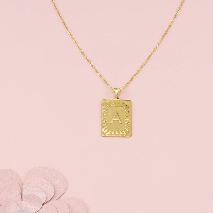 Cleopatra Monogram Letter Necklace in gold with personalized 'A' on rectangular 925 Sterling Silver pendant, on pink background.