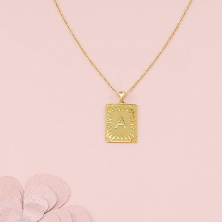 Cleopatra Monogram Letter Necklace in gold with personalized 'A' on rectangular 925 Sterling Silver pendant, on pink background.