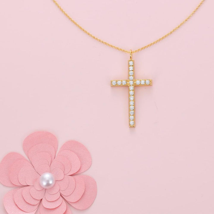 Gold crystal cross necklace with sparkling cubic zirconia stones on pink background with floral decoration