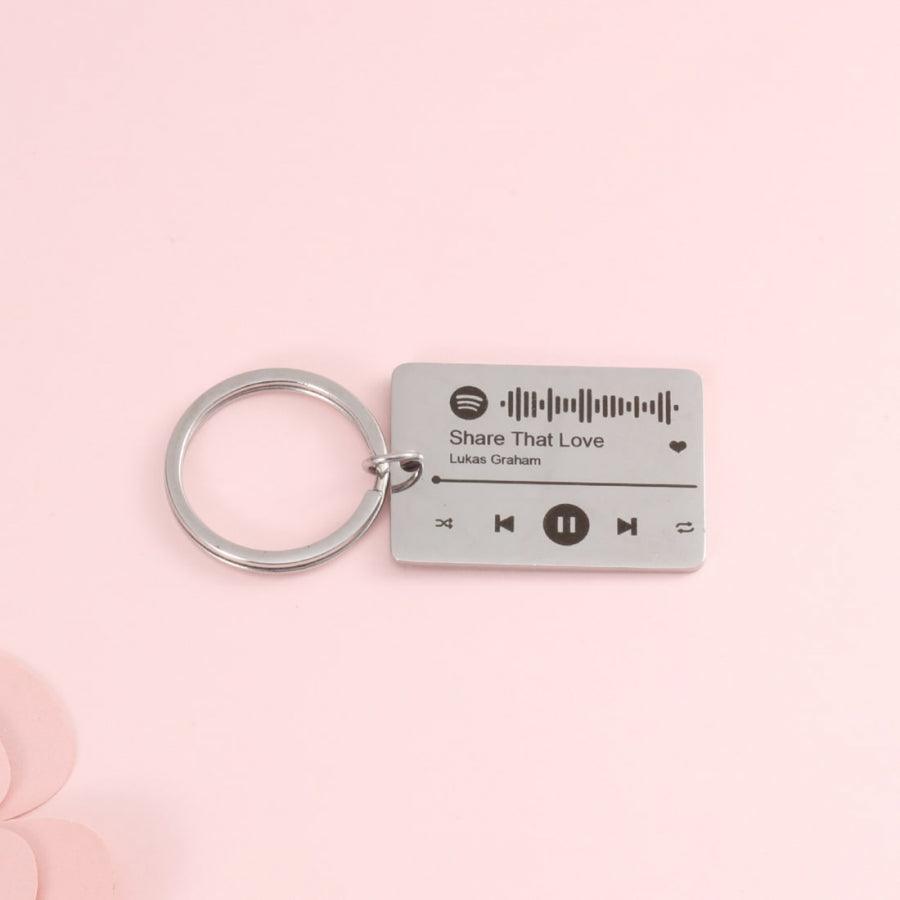 Custom Spotify Code Keychain with "Share That Love" song engraving, personalized scannable code, and music controls on a pink background.