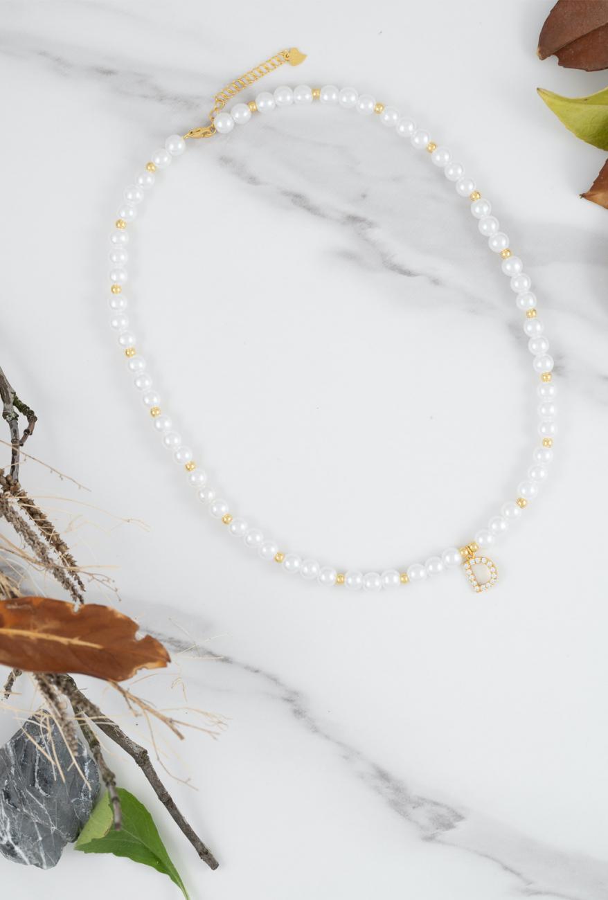 Elegant pearl necklace with zirconia-studded initial pendant on a marble background surrounded by autumn leaves