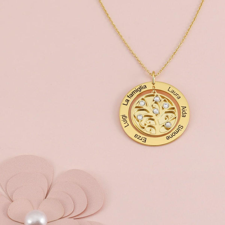 Personalized Tree of Life necklace with custom engravings and birthstones on a gold round medallion against a pink background.