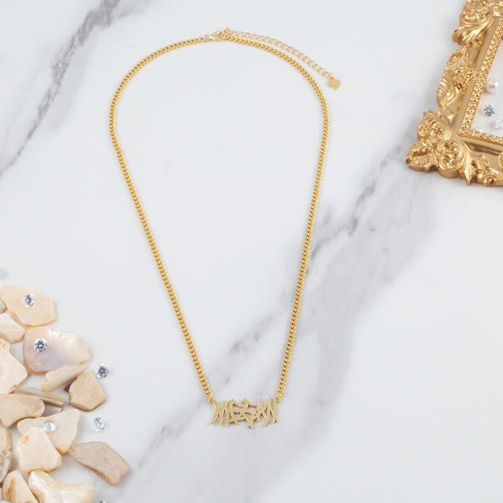 Heavy Metal Name Necklace in 18K Gold with Curb Chain on marble surface