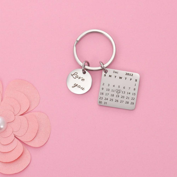 Personalized calendar keychain with engraved date and love charm on a pink background, perfect for marking special memories and occasions.