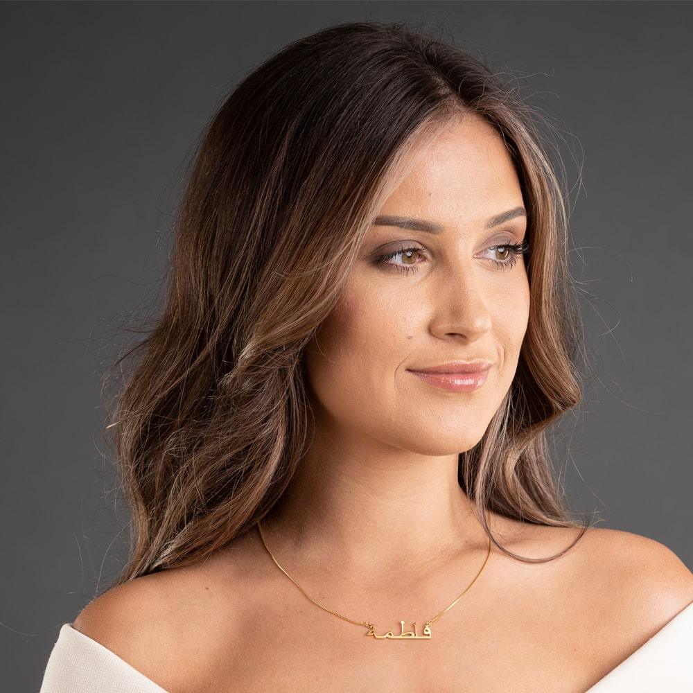 Woman wearing Arabic name necklace in 18K gold, showcasing personalized and elegant jewelry against a dark background.