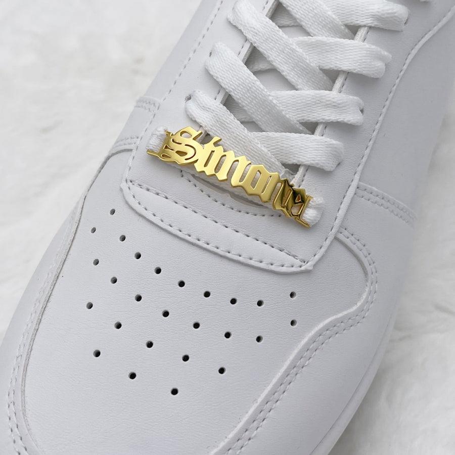 Personalized sneaker nameplate in gold attached to white sneaker shoelaces adding a unique individuality touch.